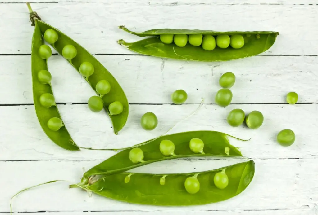 Top view of fresh green peas and pods on a rustic wooden surface, showcasing natural simplicity.